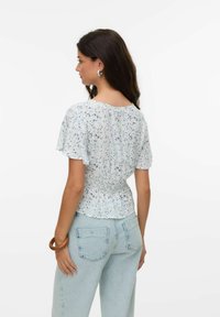 Blusa floreale azzurro chiaro con maniche corte a volant e vita arricciata. Abbinata a jeans azzurro chiaro a vita alta, in un taglio rilassato.