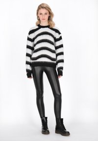 Zwart-wit gestreepte trui met een fuzzy textuur, gecombineerd met zwarte glanzende leggings en zwarte veterschoenen.