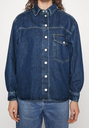 Donkerblauwe spijkerjack met knoopsluiting aan de voorkant, kraag, enkele borstzak en gerimpelde manchetten. Gladde textuur en klassieke pasvorm.