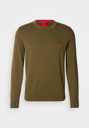 Olive green sweater in a soft knit fabric. Features a crew neck, ribbed cuffs, and a small red logo patch on the chest.