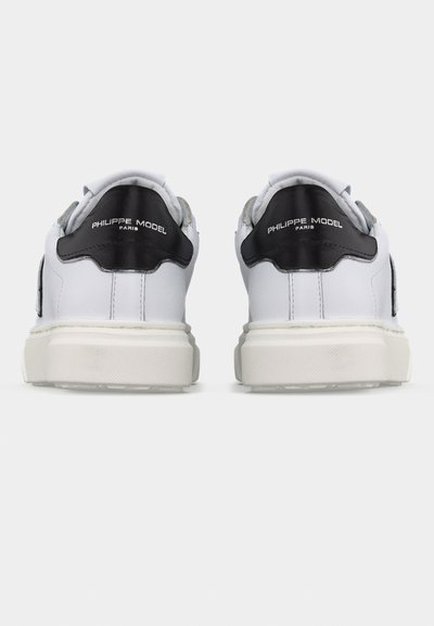 Paire de baskets blanches avec des languettes de talon noires, le logo "Philippe Model Paris" et des semelles blanches épaisses, vues de dos sur un fond blanc.
