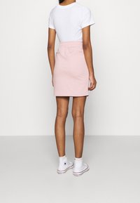 Woman wearing a white t-shirt, light pink elastic-waist skirt, and white high-top Converse sneakers standing on a plain background.