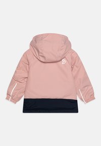 Rosa vattentät jacka med huva, med en mörkblå nederdel, elastiska ärmslut och reflexdetaljer. Märkbart logotyp på ryggen.