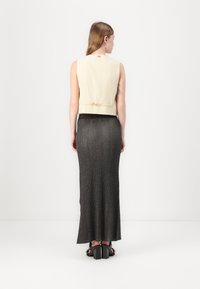 Ljus beige kort väst med en bakgående rosett, tillsammans med en lång, mörk, ribbad kjol med en slät textur och lätt glans.