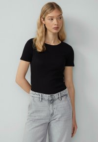 Zwarte geribbelde top met korte mouwen, gecombineerd met lichtgrijze high-waisted jeans. De top heeft een ronde halslijn; de jeans hebben een ontspannen pasvorm en zichtbare naden.