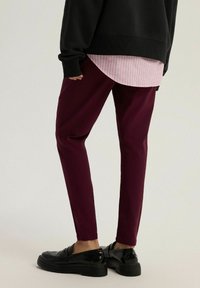 Burgundowe spodnie o slim fit, uszyte z gładkiego materiału. W połączeniu z czarnym, oversize'owym swetrem i różową koszulą w paski pod spodem.