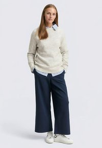 Hele beež villane kampsun, mille all on sinise ja valge triibulise särgi kiht, kombineeritud laia lõikega tumesiniste pükstega ja valgete tennistega. Lihtne disain, mugav lõige.