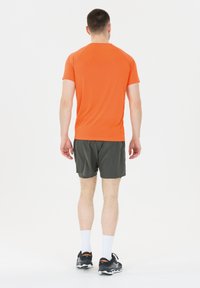 Oranssi lyhythihainen urheilusukka, yhdistettynä tummanvihreisiin shortsihin, mustat lenkkarit ja valkoiset urheil SOCKit. Takakatsaus.