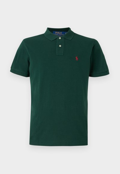 Grön polo t-shirt i bomull, med klassisk krage, två vita knappar och en liten röd logotyp på vänster bröst. Korta ärmar.