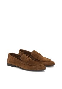 Mocassins en daim marron avec une semelle plate, présentant un bout cousu et une large bride sur le cou-de-pied. Texture lisse et design classique.