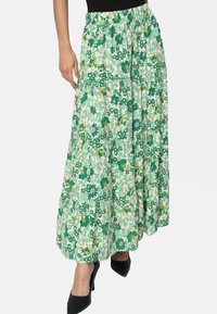 Jupe maxi florale dans des tons de vert avec un design à volants, fabriquée en tissu léger. Dispose d'une taille froncée et de motifs de diverses plantes.