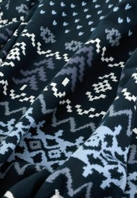 Knitted fabric featuring a dark blue background with varying geometric patterns in light blue, gray, and white. Soft texture with layered appearance.