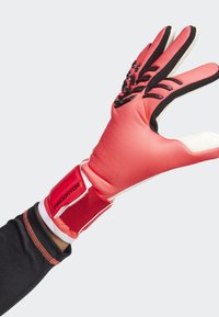 Rode doelmanhandschoen met een gestructureerde grip op de vingers, zwarte accenten en een klittenbandsluiting met het label "PREDATOR" rond de pols.