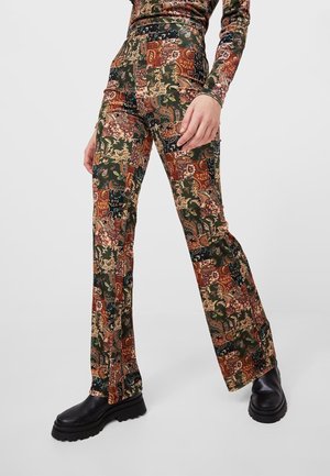 Personne portant un pantalon taille haute évasé avec des motifs floraux multicolores complexes en patchwork et des bottes noires à semelles épaisses.