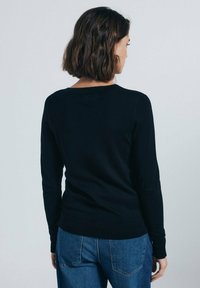 Maglione nero a maglia con maniche lunghe e scollatura a girocollo, design aderente, polsini e orlo a costine. Indossato con jeans blu, che mostrano la vista da dietro.