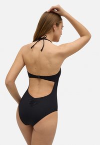 Bañador negro de una sola pieza con cuello halter, espalda descubierta y detalle fruncido en la cintura. Fabricado con tela suave y elástica.