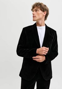 Melnas zīda žakete ar satīna atlokiem, vienu pogu un smalkām kabatām. Apakšā valkāta balta T-kreklu.