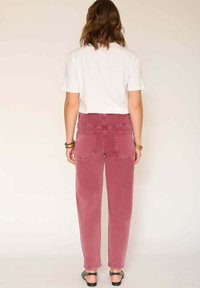 Jean en denim rose taille haute et ample avec deux poches arrière, porté avec un t-shirt blanc à manches courtes et des sandales noires.