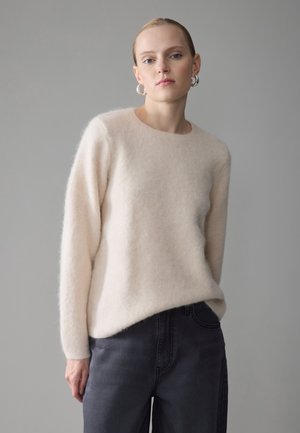 Maglione di lana rosa chiaro con maniche lunghe e scollo rotondo, indossato sopra jeans scuri. La texture sembra morbida e leggermente pelosa.