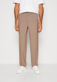 Gaiši brūnas pielāgotas bikses ar gludu tekstūru, ar plakanu priekšpusi un jostas cilpām. Kombinētas ar baltām sporta kurpēm.