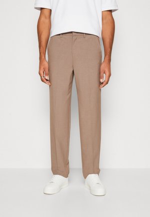 Bež hlače narejene po meri z ravnim krojem, ki imajo subtilno teksturo in dva sprednja žepa. V kombinaciji z belimi supergami.