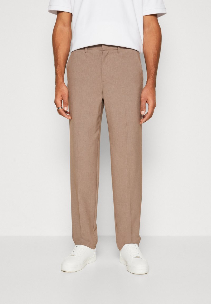 Gaiši brūnas pielāgotas bikses ar gludu tekstūru, ar plakanu priekšpusi un jostas cilpām. Kombinētas ar baltām sporta kurpēm.