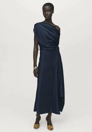 Navy draped satin dress with asymmetric hem and one-shoulder design. Model wears brown heeled sandals and a metallic bracelet on one wrist.