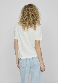 Camiseta blanca de manga corta con un ajuste relajado, tejido texturizado y dobladillo redondeado. Modelo combinado con jeans de mezclilla azul claro.
