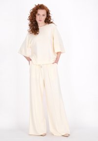 Krémové široké kalhoty a odpovídající oversized top vyrobený z měkké látky, který má uvolněný střih a jemné designové detaily.