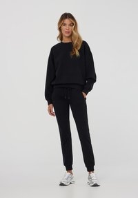 Felpa nera e pantaloni coordinati in tessuto morbido, con una vestibilità rilassata, polsini a coste e vita regolabile con cordino.