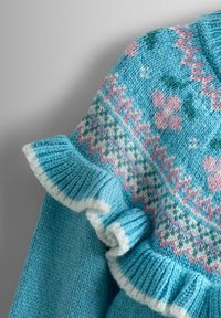 Strickpullover in Hellblau mit floralem Muster in Pink und Grün. Verfügbar mit Rüschen an den Ärmeln und am Halsausschnitt. Weiche Textur, lebendige Farben.