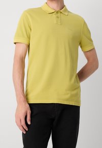 Polo en coton jaune clair avec col, manches courtes et patte à deux boutons. Logo brodé discret sur la poitrine.