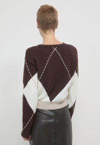 Maglione con motivo argyle marrone e bianco, dalla texture morbida, vestibilità rilassata e orlo beige chiaro. La vista posteriore mostra dettagli a diamante e a linee.