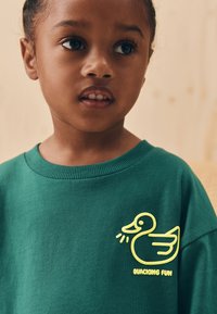 Grøn sweatshirt med et gult broderet ande-motiv og teksten "QUACKING FUN", rund halsudskæring og blød tekstur.