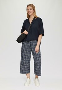 Marineblauwe blouse met korte, brede mouwen, gecombineerd met gemusterde culottes in blauw en wit. Witte chunky sneakers en een kleine zwarte crossbody tas.