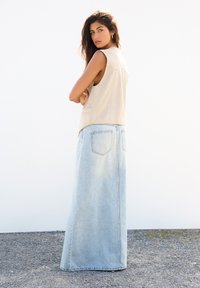 Beige ärmellose Lederweste kombiniert mit einem langen, hellblauen Denim-Rock. Der Rock verfügt über Gesäßtaschen und hat eine lockere Passform.