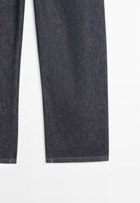 Dunkelblaue Jeanshosenbeine mit sichtbarer Naht am Saum, dargestellt vor weißem Hintergrund.