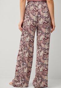 Losse pyjamabroek in een maroon en crèmekleurig paisleypatroon, met een elastische tailleband en gemaakt van een lichtgewicht stof.