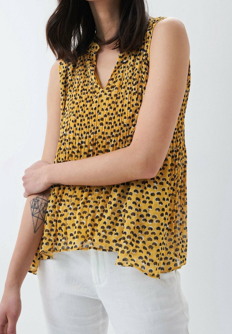 Žlutá halenka bez rukávů s plisovaným designem, zdobená černými a hnědými abstraktními vzory. Lehká průsvitná látka, výstřih do V.