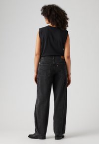 Zwarte mouwloze top gecombineerd met hoge, loose-fit zwarte jeans. De jeans hebben klassieke achterzakken en een leren logo.