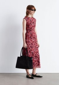 Rotes, floral gemustertes, tailliertes Kleid mit einem gerafften Bund, kombiniert mit einer schwarzen Wildleder-Tasche und schwarzen Ballerinas. Das Model trägt Sonnenbrillen.