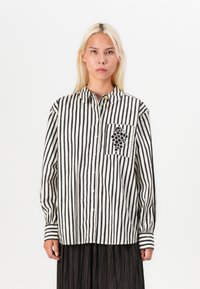 Camicia a maniche lunghe con strisce bianche e nere, con bottone e taschino con ricamo di tralcio d'uva e colletto classico.