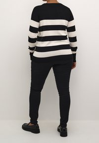Pull à rayures noires et blanches en matière douce, associé à un pantalon skinny noir et des chaussures noires, vu de dos.