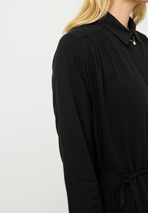 Robe noire avec un col, des détails de boutons, des plis aux épaules et une ceinture à nouer. Tissu lisse, manches longues et design simple.