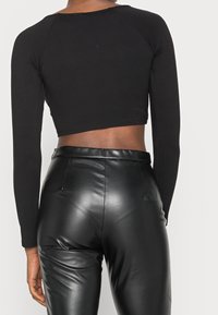 Mustahiilinen musta pitkähihaine crop-top, jossa on pyöreä kaula-aukko, yhdistettynä korkeavyötäröisiin mustiin tekonahkahousuihin, jotka ovat sileitä ja kiiltäviä.