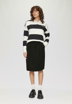 Poloshirt met lange mouwen in zwart-witte strepen, met een ritskraag. Gecombineerd met een zwarte rok tot op de knie en zwarte platform schoenen.