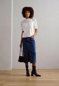 Hvid bluse med teksturerede puffærmer, parret med en mørk denim kjoleskørt i mellemlængde med en frontslids og sorte ankelstøvler.
