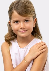 Goldenes Armband mit kleinen Charms, das am Handgelenk eines Kindes getragen wird. Das Kind hat schulterlanges welliges Haar und trägt ein hellrosa Oberteil.