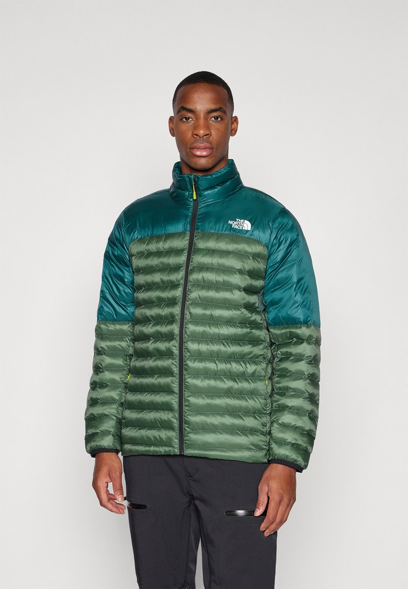 Nafukovací zelená a tyrkysová bunda s vysokým límcem, zipovým zapínáním a logem The North Face. Má horizontální švy a elastické manžety.