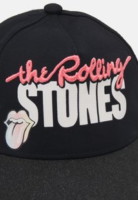 Svart baseballcap med brodert "the Rolling Stones" i rosa, fet skrift, med en hvit tunge-logo på frontpanelet.